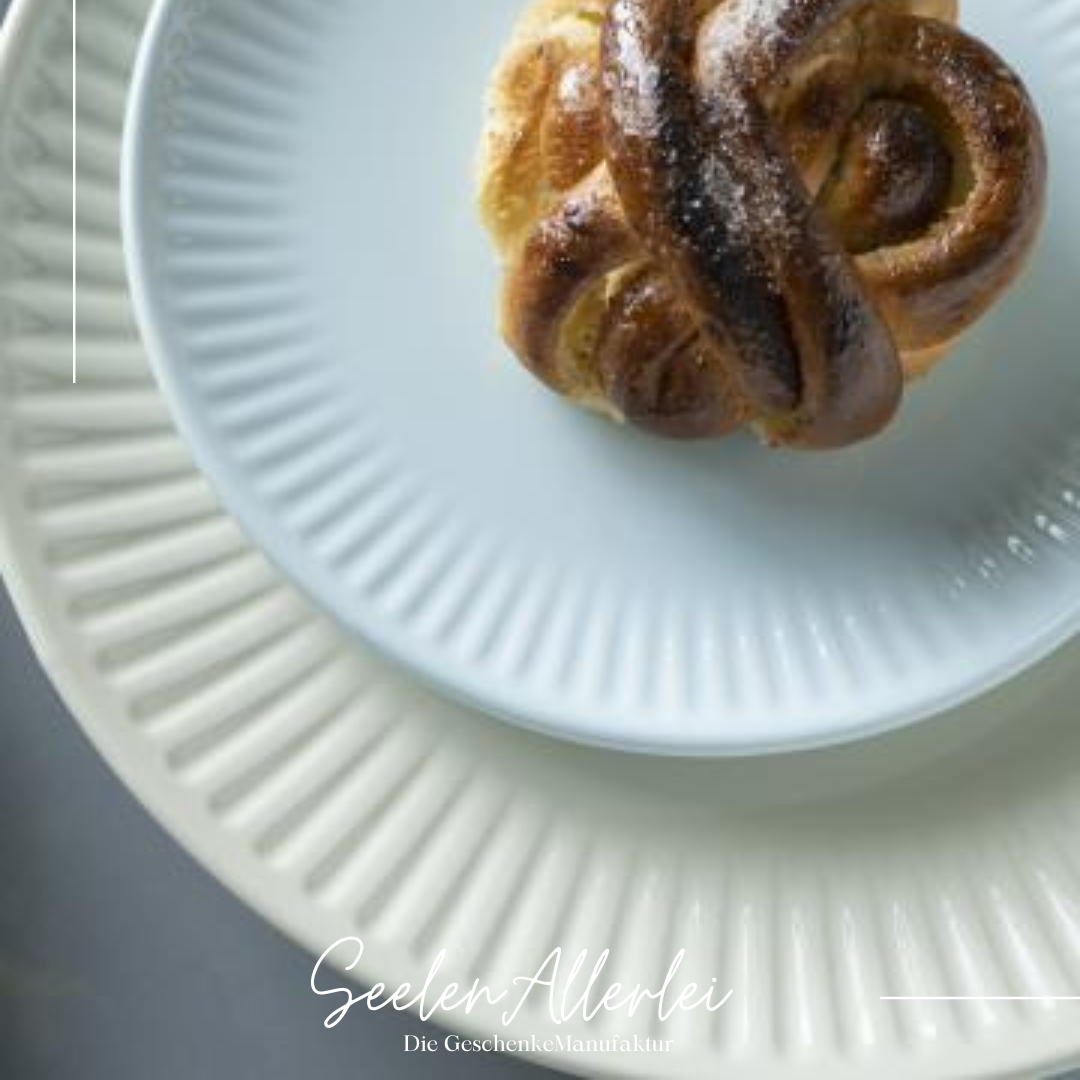 auf einem beige farbenen Essteller liegt ein weißer Frühstücksteller mit einem französichen Brötchen drauf