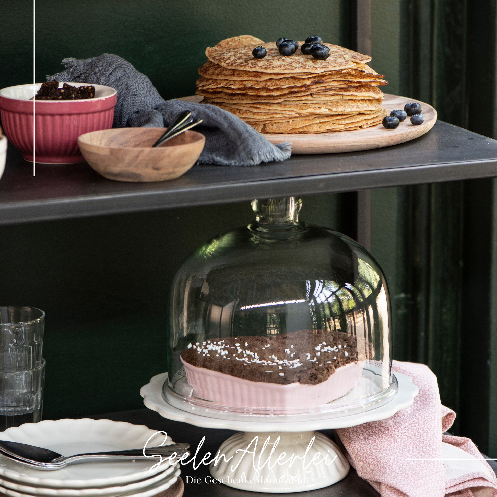 in einem Regal stehen Teller und Tortenplatte mit Glasabdeckug und auch schalen mit Pancakes