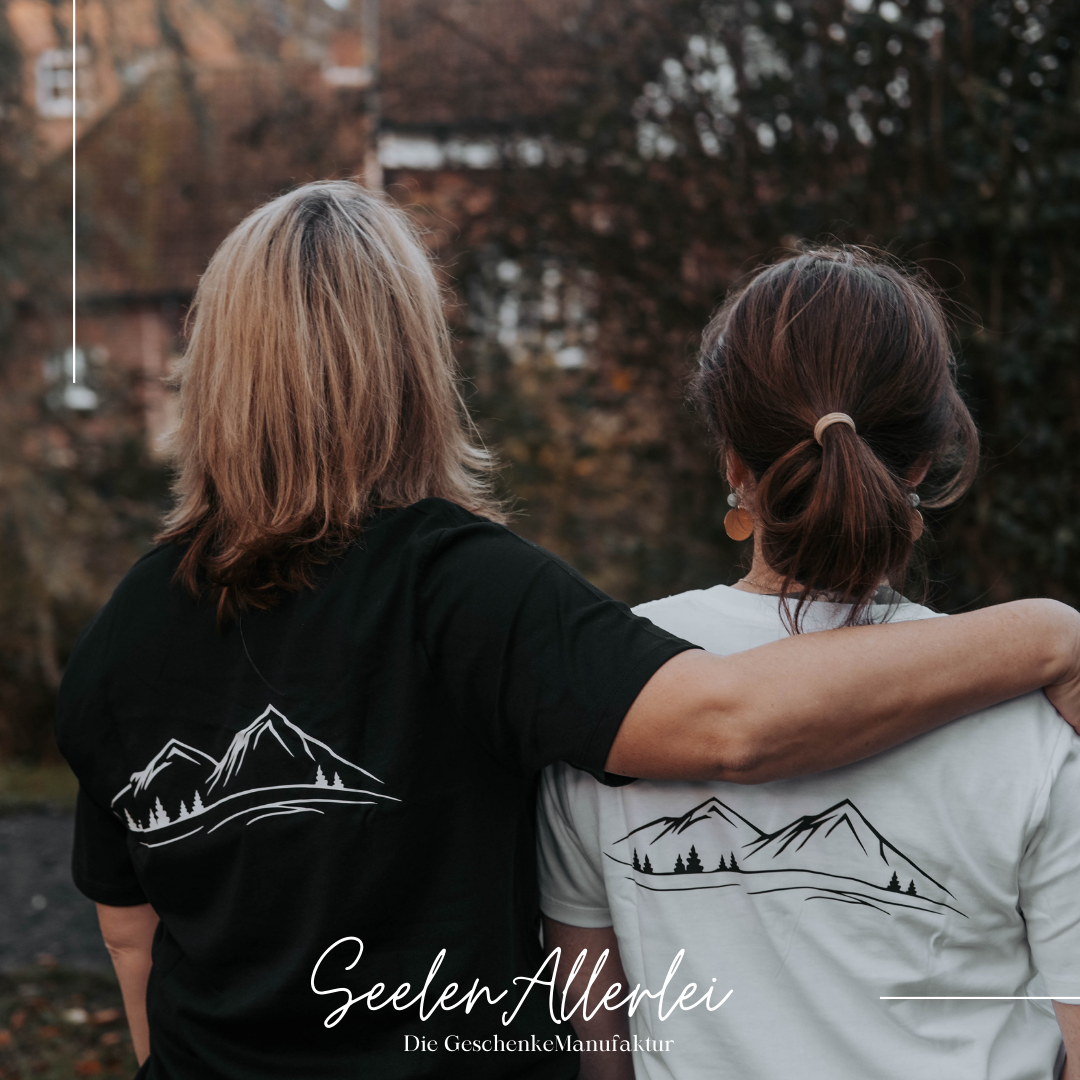 Diana und Marina als Inhaber der GeschenkeManufaktur stehen Arm in Arm vor dem Walkenbrückentor in Coesfeld jeweils mit einem schwarzen und weißem Shirt mit einer Bergsilhouette drauf