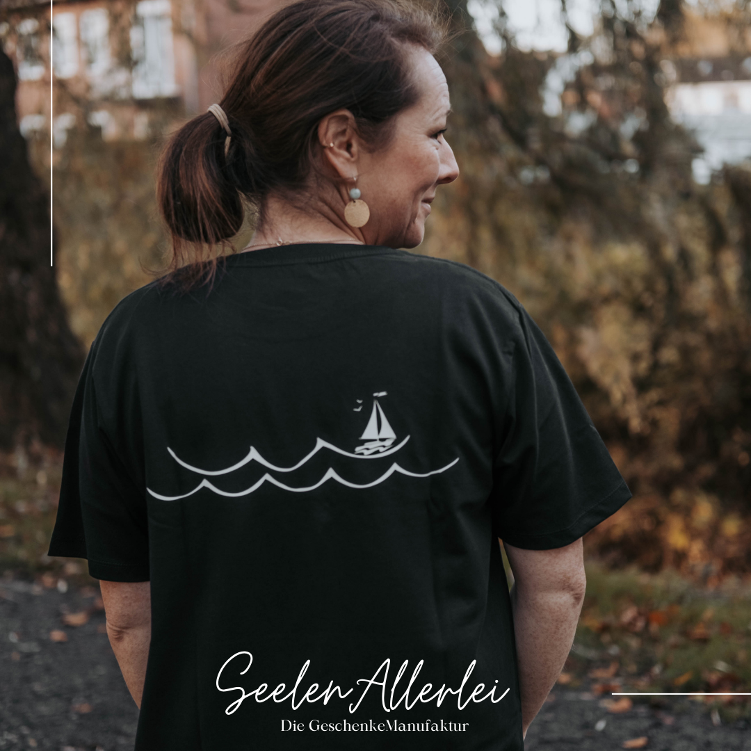 Eine Frau trägt das lifestyle Shirt mit Wellenprint und einem Segelboot auf dem Rücken