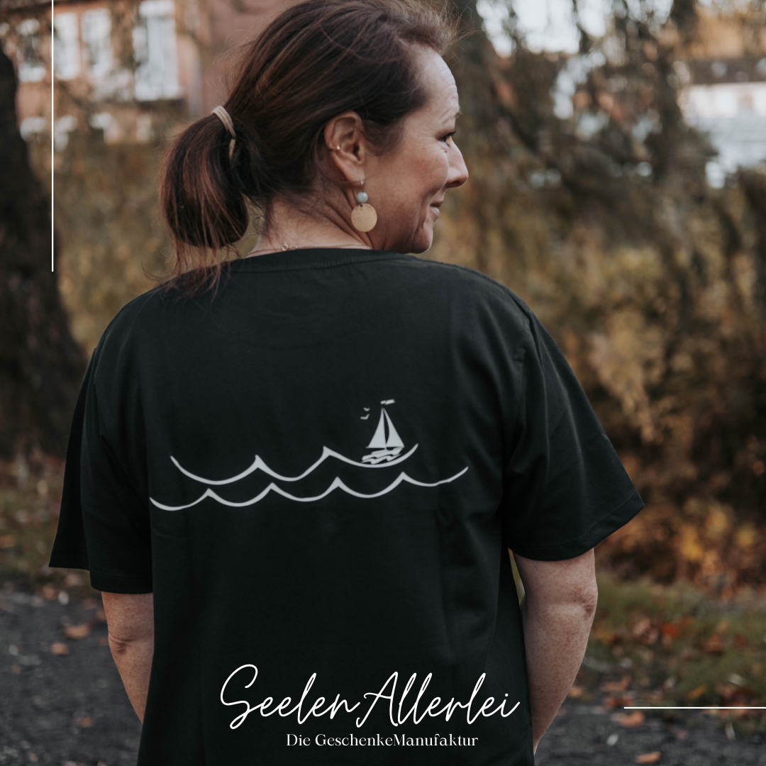 Eine Frau mittleren Alters trägt das Shirt mit dem Rückenprint Wellen und Segelboot in einem Park