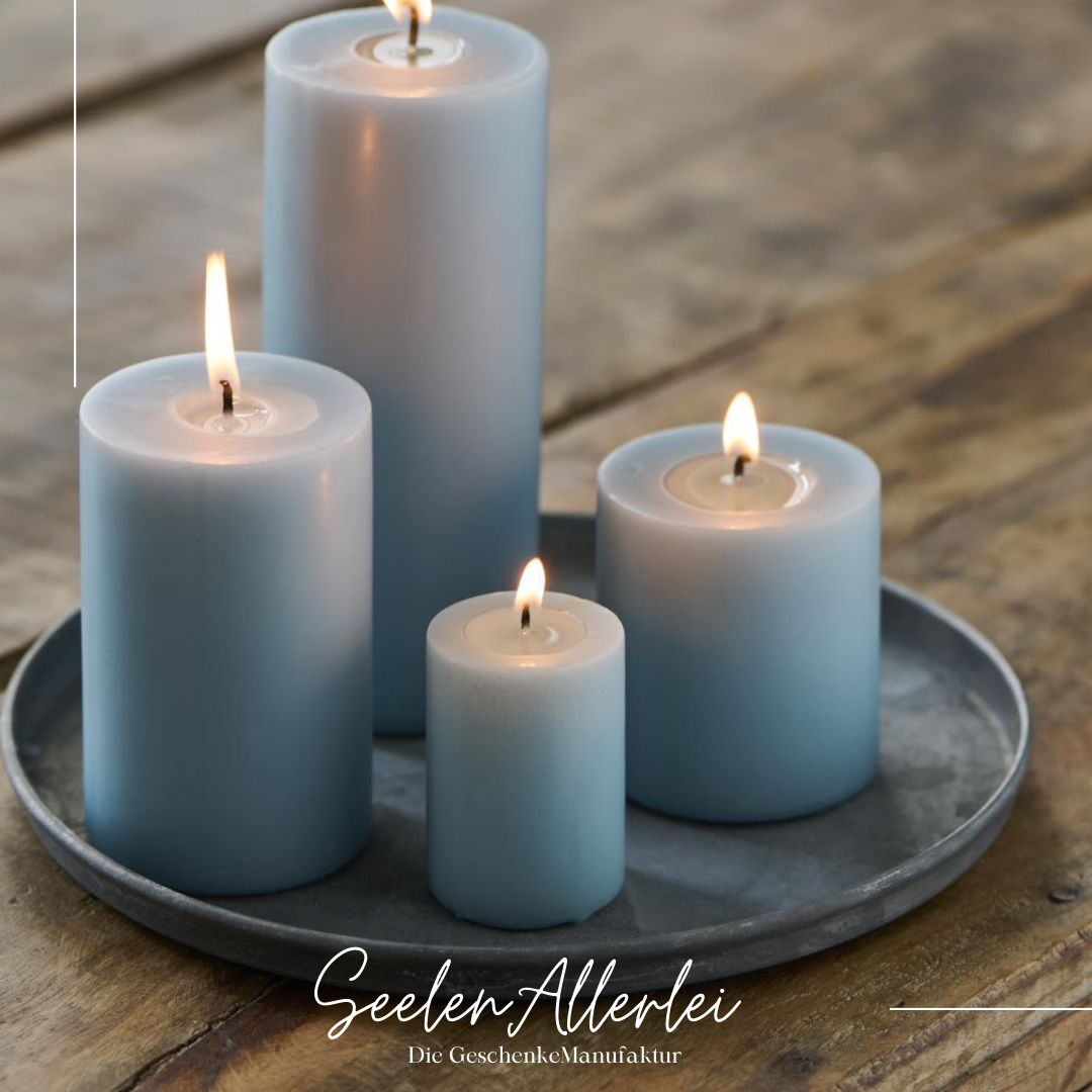 Arrengement aus 4 verschieden großen angezündeten Kerzen, die auf einem großen Tablett in zinkoptik auf einem Holztisch stehen.