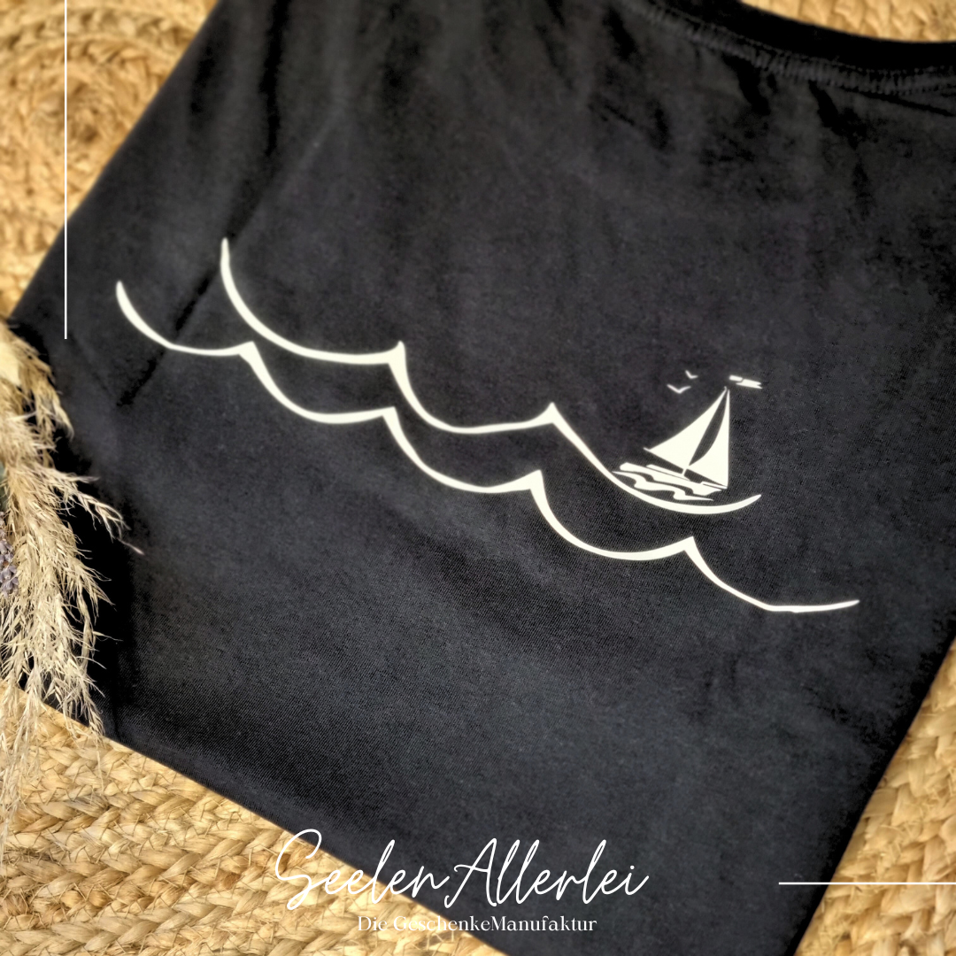 Aufdruck von Wasserwellen und einem Segelboot hinten auf einem schwarzen Shirt. In die Wellen kann der Name geschrieben werden